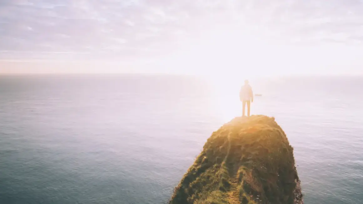Ein Mensch steht auf einer Klippe am Meer, die Sonne blendet. Was tun bei einer Lebenskrise? Der Blick in die Weite gibt Hoffnung.