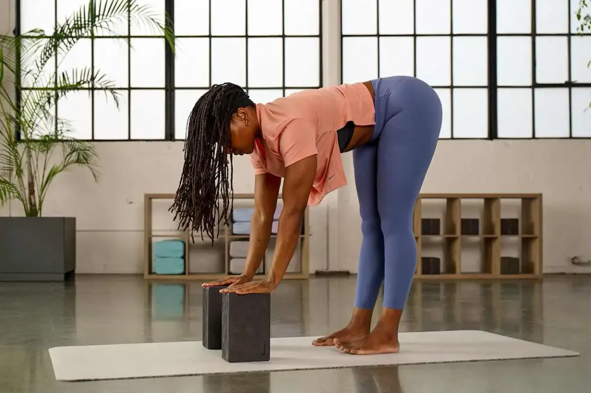 Frau mit Dreadlocks praktiziert Yoga mit Block. Sie beugt sich vor, Hände auf zwei Blöcken, um die Dehnung zu vertiefen.