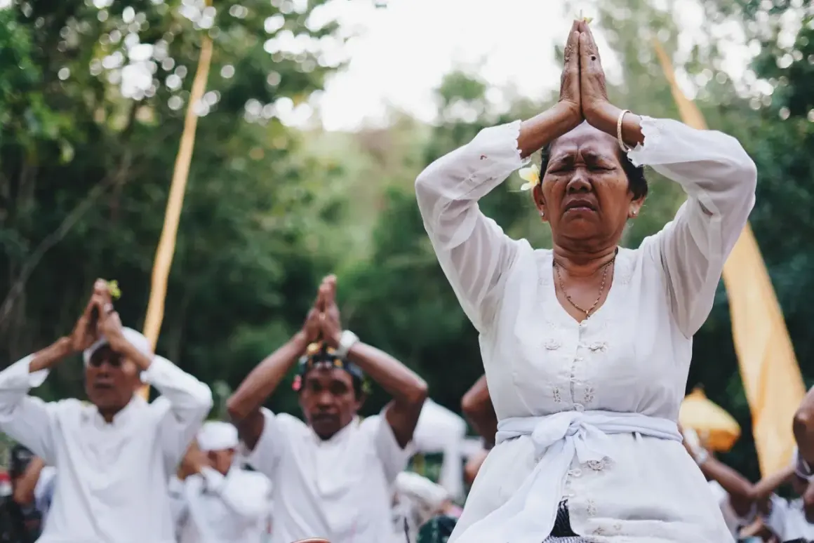 Frauen und Männer in Weiß beten mit gefalteten Händen. Die Namaste-Bedeutung von Respekt und Ehrfurcht wird in dieser spirituellen Zeremonie ausgedrückt.