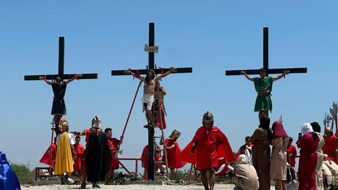 Nachstellung, wie Jesus stirbt am Kreuz, mit zwei weiteren Männern, die ebenfalls gekreuzigt werden. Soldaten in römischer Kleidung und Zuschauer sind anwesend.