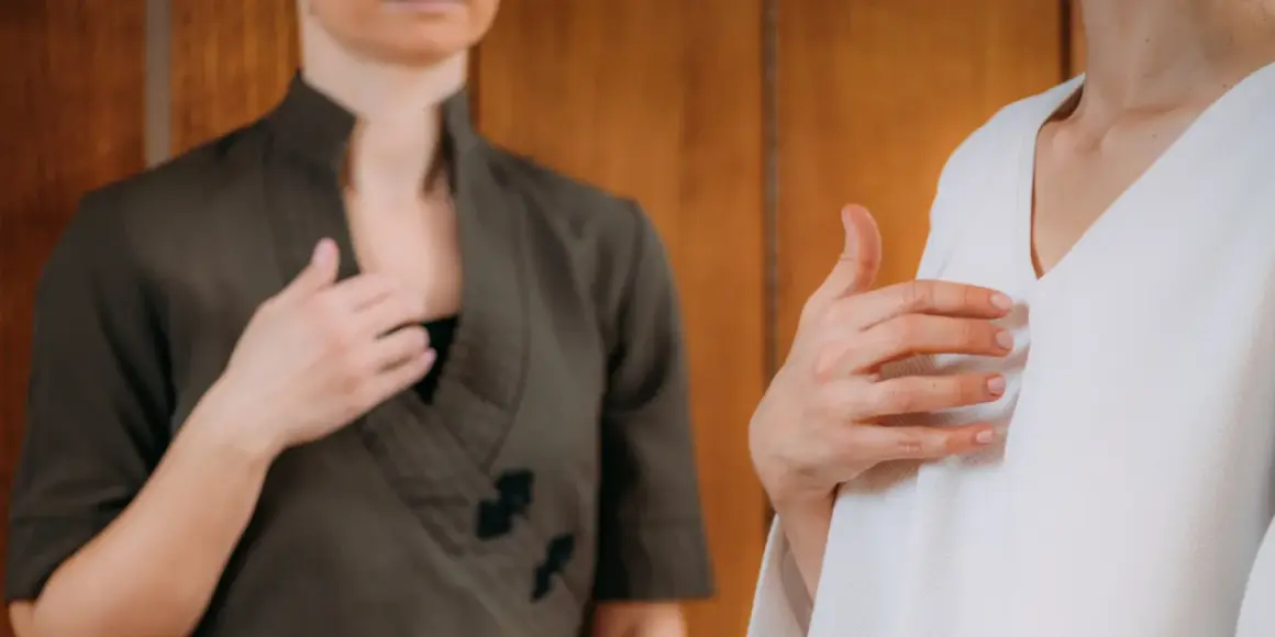 Zwei Frauen üben Klopftechnik zur Linderung von Angst. Eine hält die Hand auf der Brust, die andere auf dem Oberarm.