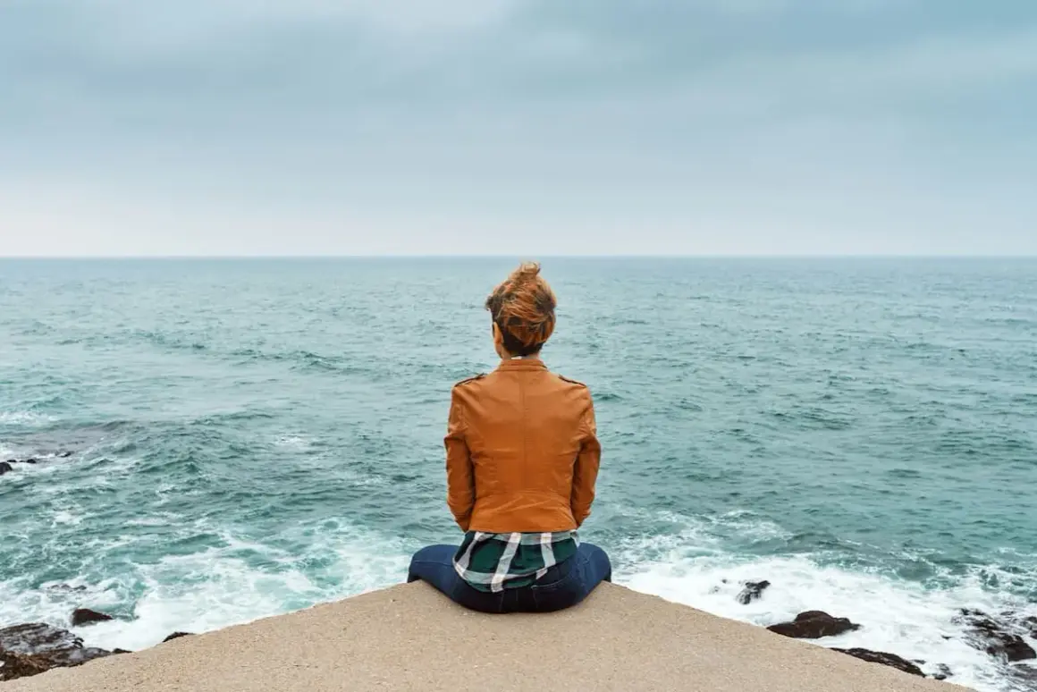 Frau sitzt am Meer, blickt in die Ferne und denkt über wichtige entscheidungen im leben nach.