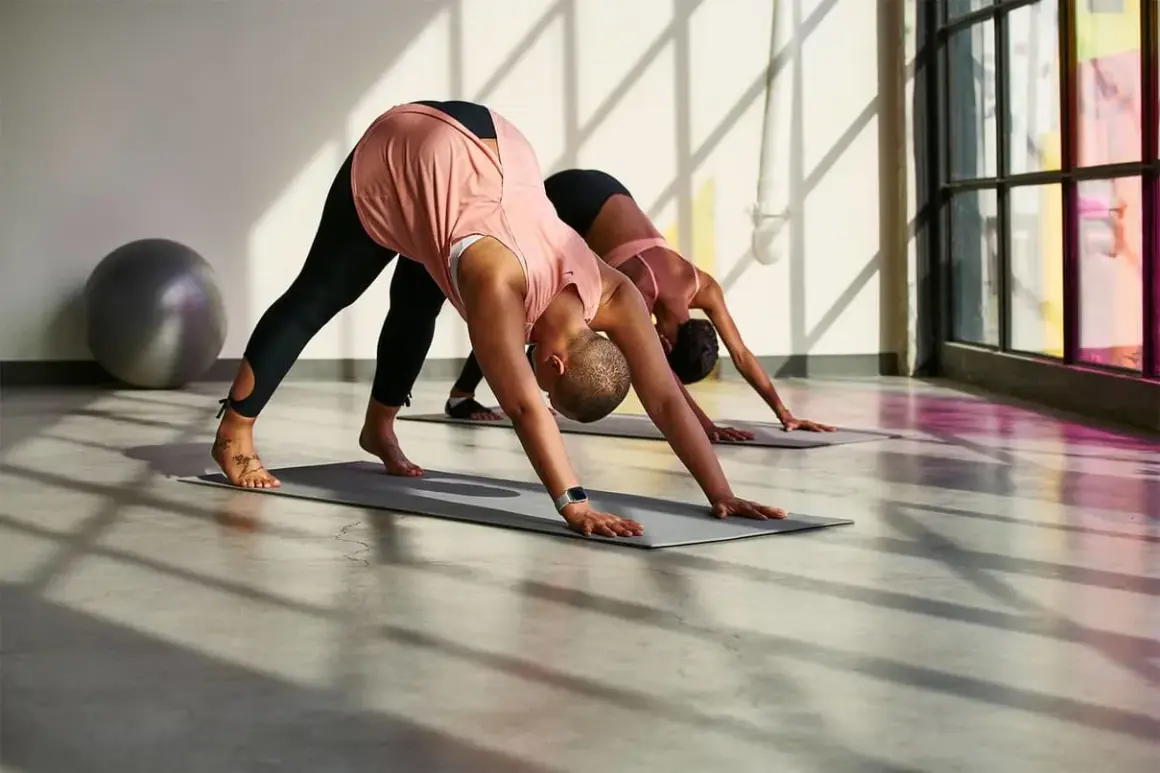 Zwei Frauen machen Yoga im Herabschauenden Hund, die Beine sind ausgestreckt.
