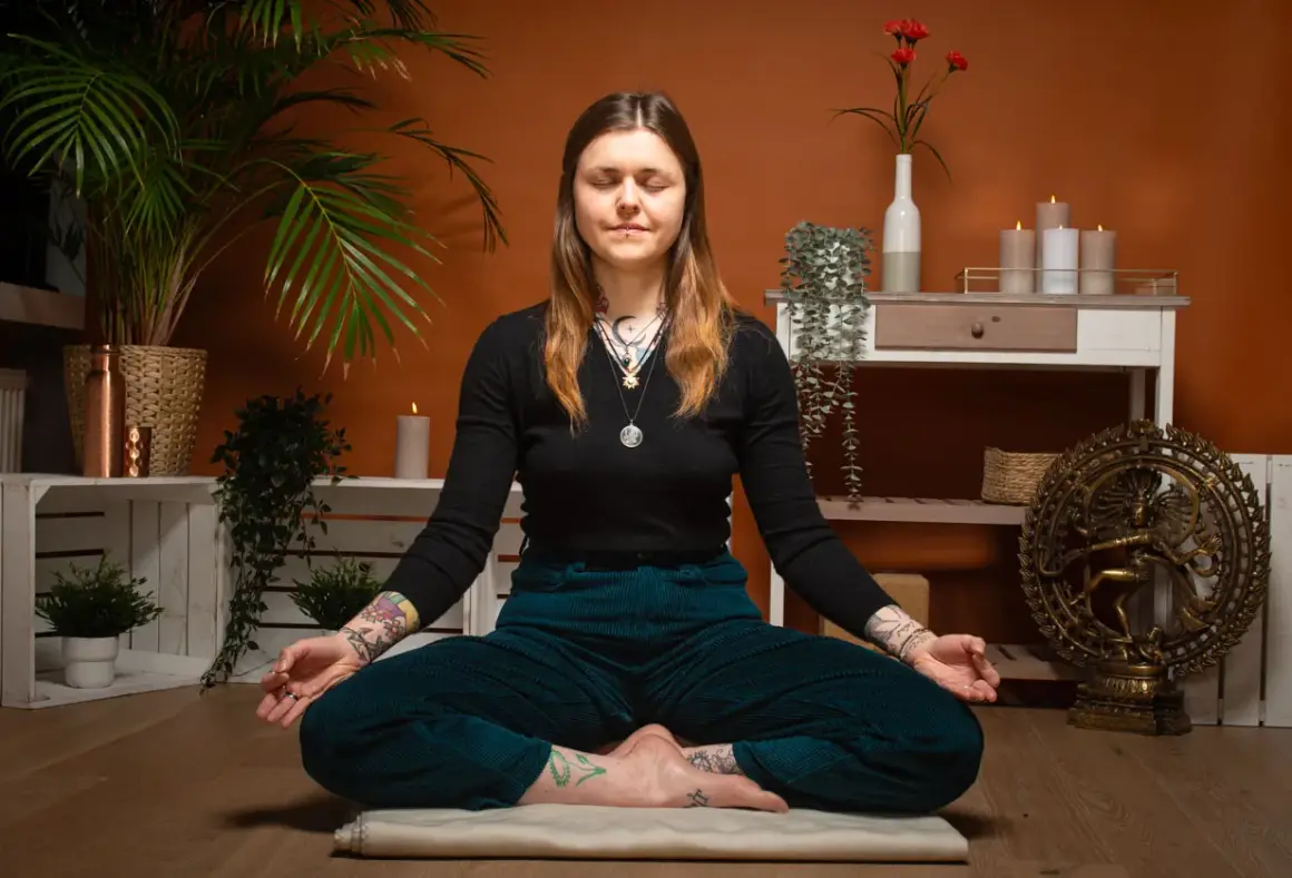 Frau in tiefer meta meditation, umgeben von Pflanzen und Kerzen. Eine Shiva-Statue im Hintergrund.