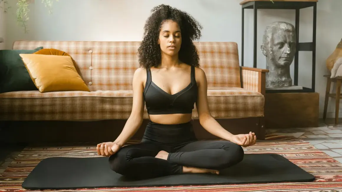 Frau in schwarzer Sportkleidung praktiziert Krafttier Meditation auf einer Matte. Sie sitzt im Lotussitz, Augen geschlossen, Hände im Mudra.