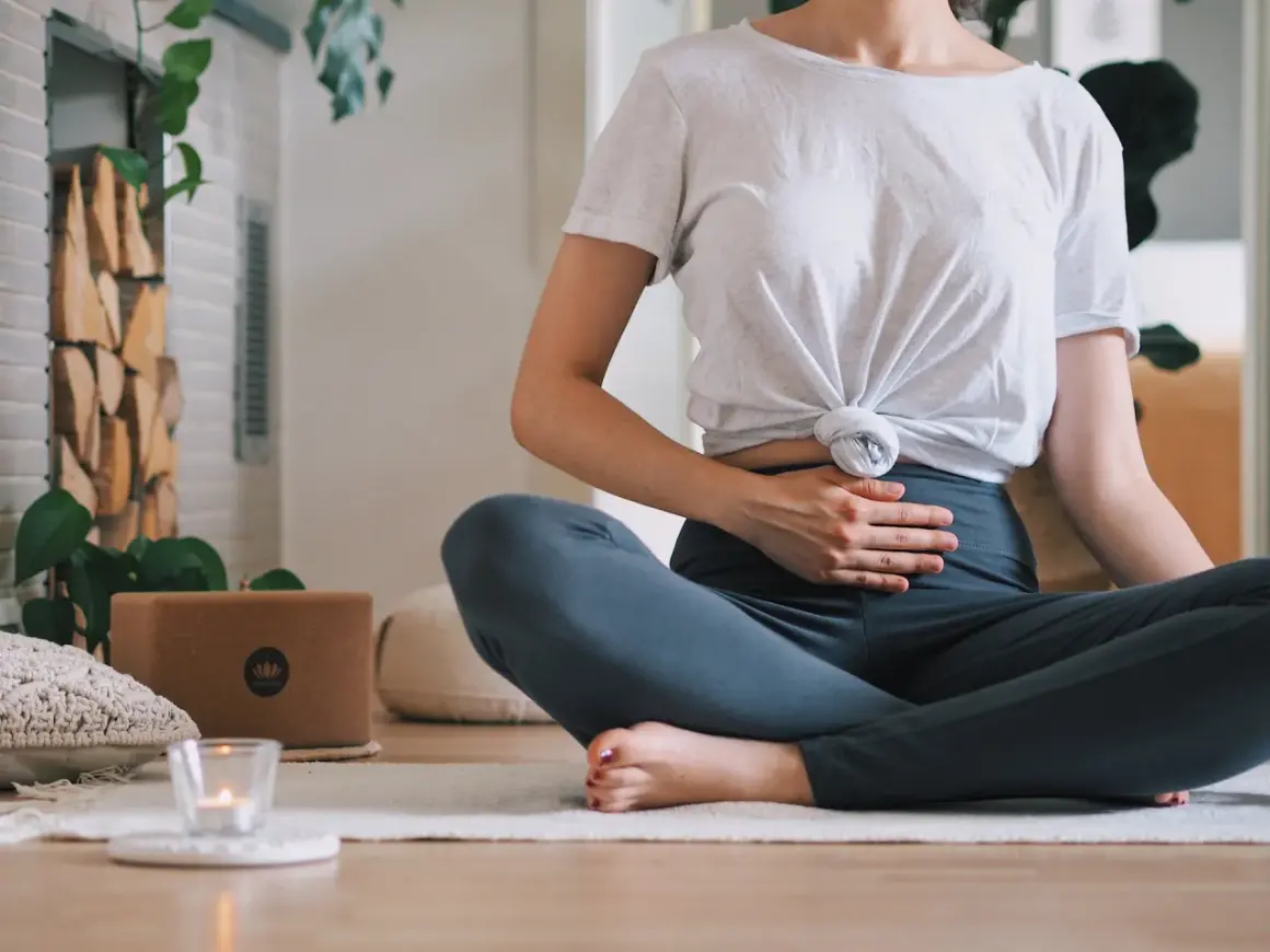 Frau in Lotussitz übt Kapalabhati Pranayama, Hände auf dem Bauch, um die Bauchatmung zu spüren.