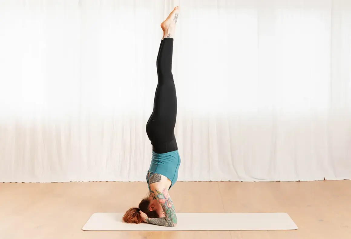 Frau in Kopfstand-Yoga-Pose auf Matte. Die Wirkung dieser Haltung ist belebend und kräftigend.