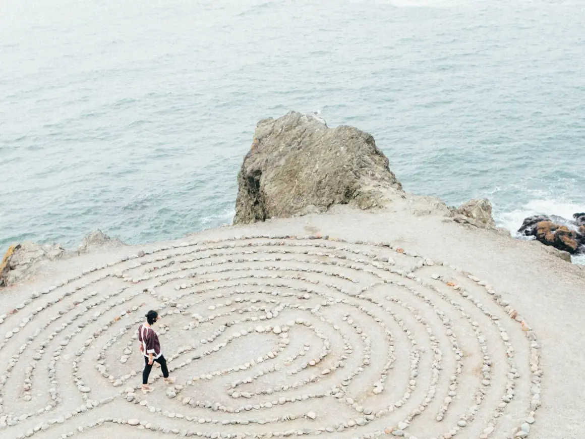Person geht durch einen Steinlabyrinth am Meer. Ein Symbol für die Ausbildung zum spirituellen Coach, die Suche nach innerer Klarheit.