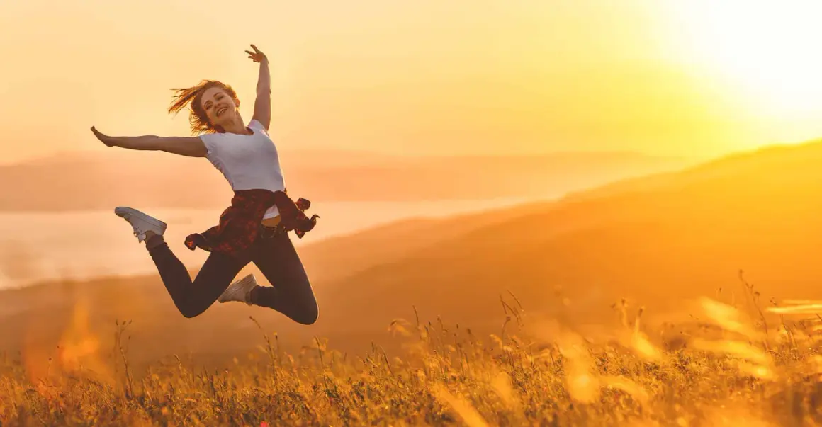 Eine Frau springt voller Freude in der goldenen Abendsonne. Sie ist voller Energie und genießt den Moment in der Natur.