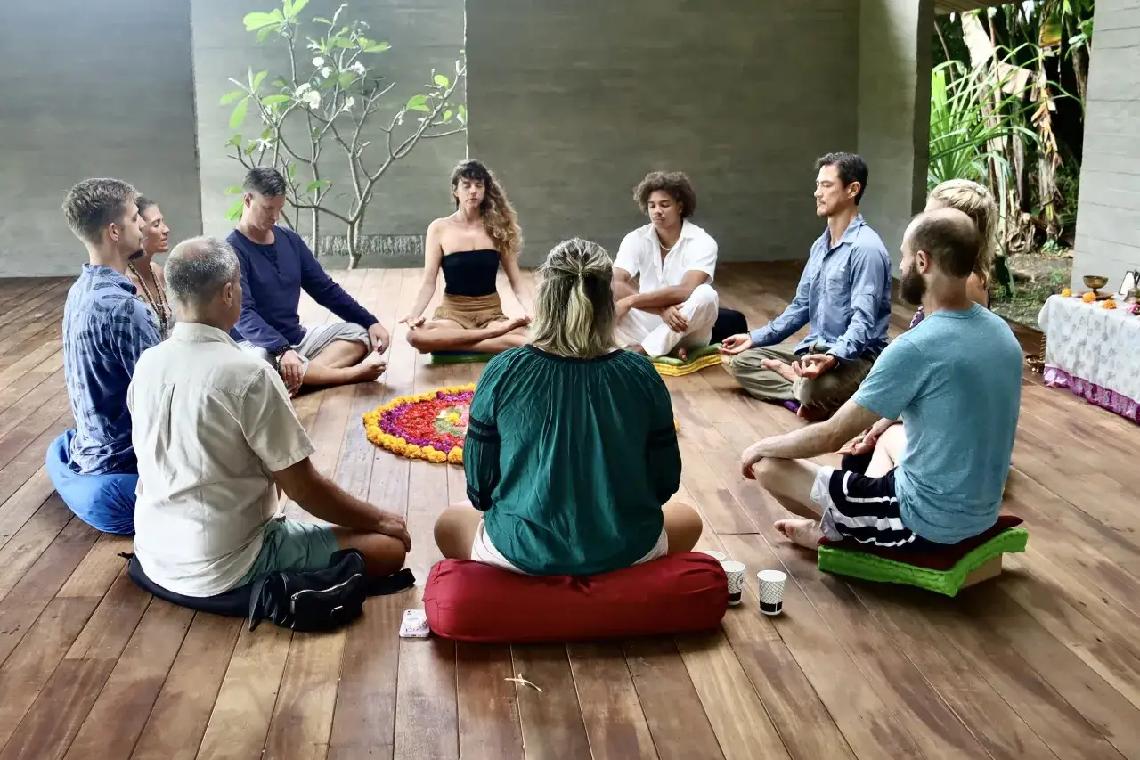 Menschen sitzen im Kreis auf dem Boden, umgeben von einer Blumenmandala. Sie scheinen an einer Meditationssitzung teilzunehmen, vielleicht f&uuml;r einen Ayurveda Podcast.