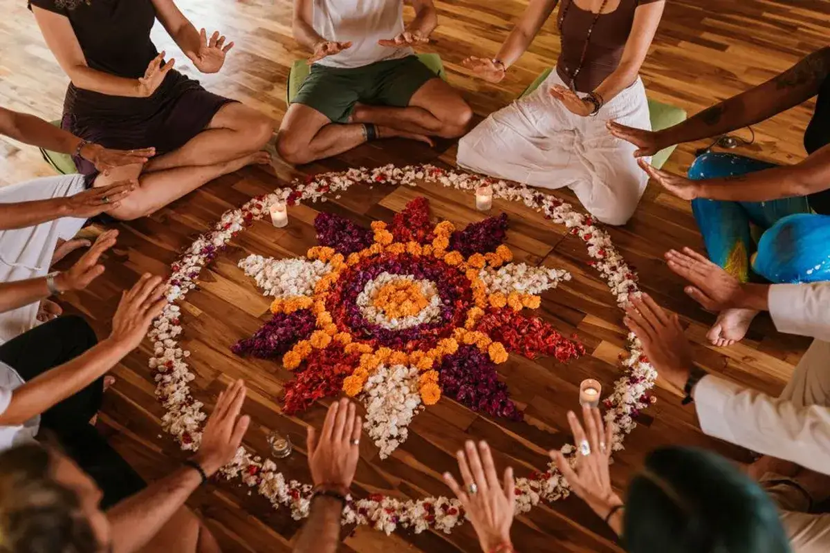 Menschen sitzen im Kreis um ein Blumenmandala. H&auml;nde sind erhoben, als ob sie die Energie von Vipassana sp&uuml;ren.