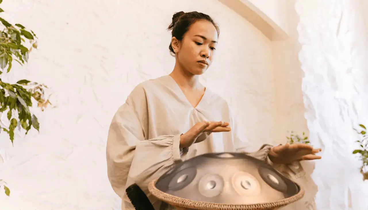 Frau bei einer Klang Meditation, die mit den H&auml;nden &uuml;ber einem Handpan-Instrument schwebt.