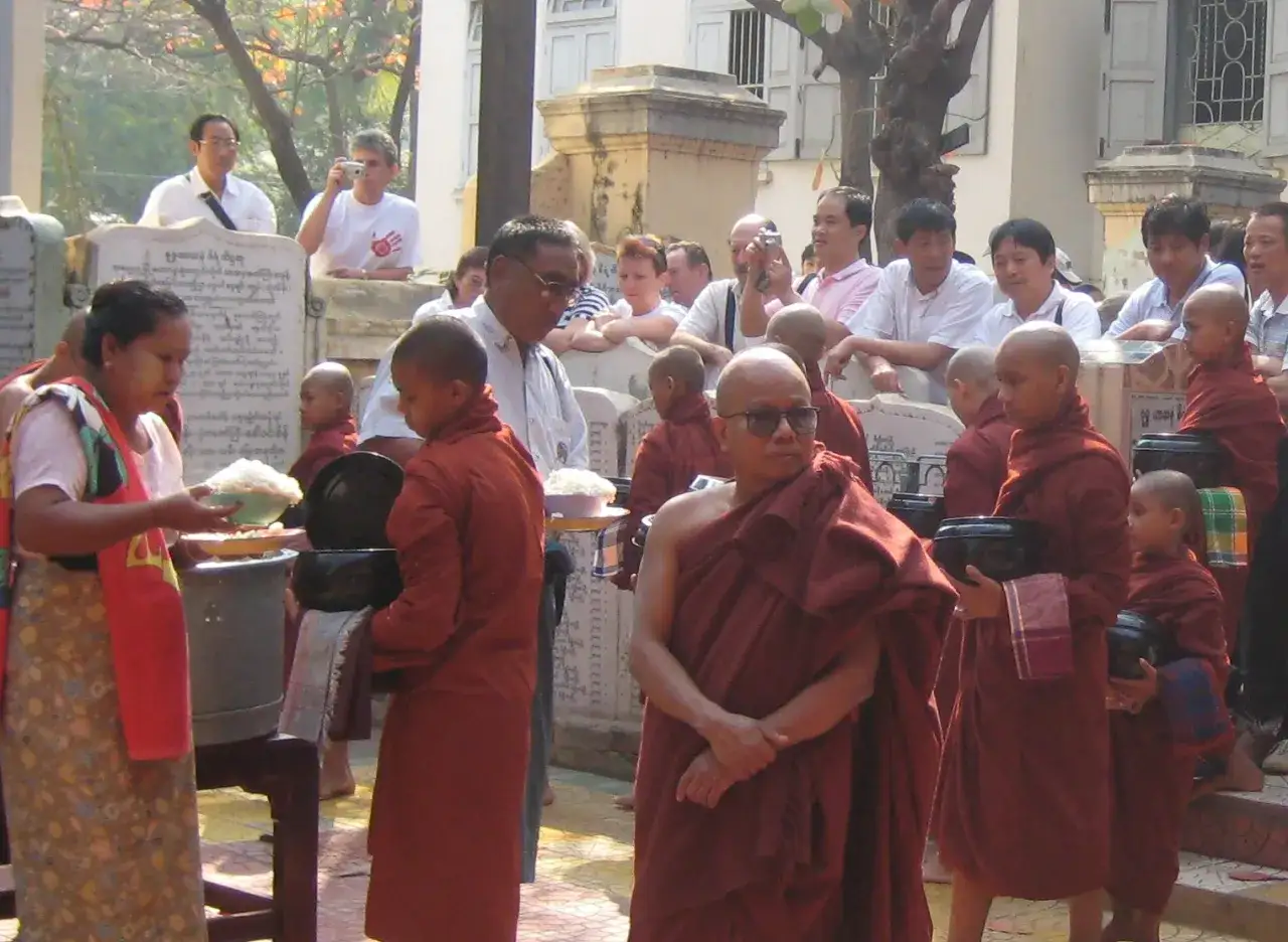 Mönche in safranfarbenen Roben erhalten Spenden. Einblicke, wie leben Buddhisten im Alltag, mit Opfergaben und Gebeten.
