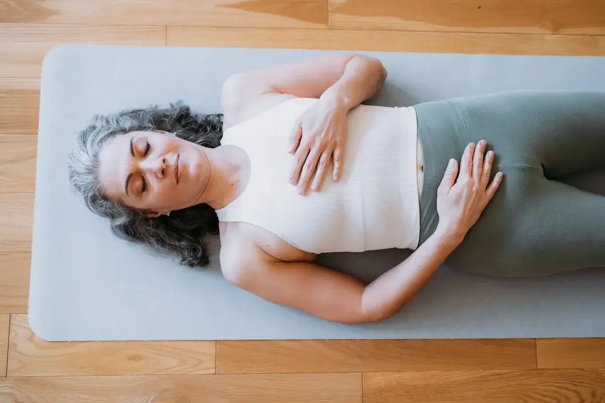 Frau in entspannter Pose, H&auml;nde auf Brust und Bauch, genie&szlig;t eine Meditation im Liegen auf einer Matte.