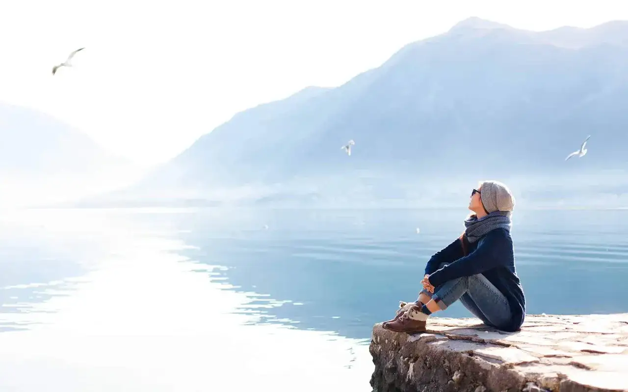 Frau sitzt am Wasser, blickt in die Ferne und lässt die Gedanken schweifen. Zeit, overthinking stoppen und die Ruhe genießen.