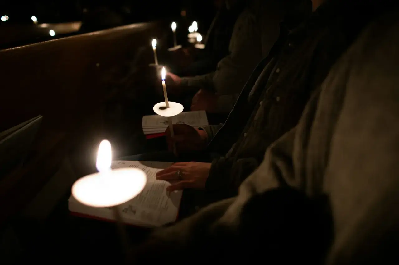 Kerzenlicht erhellt eine Vigil Kirche. Menschen halten brennende Kerzen und lesen in B&uuml;chern.