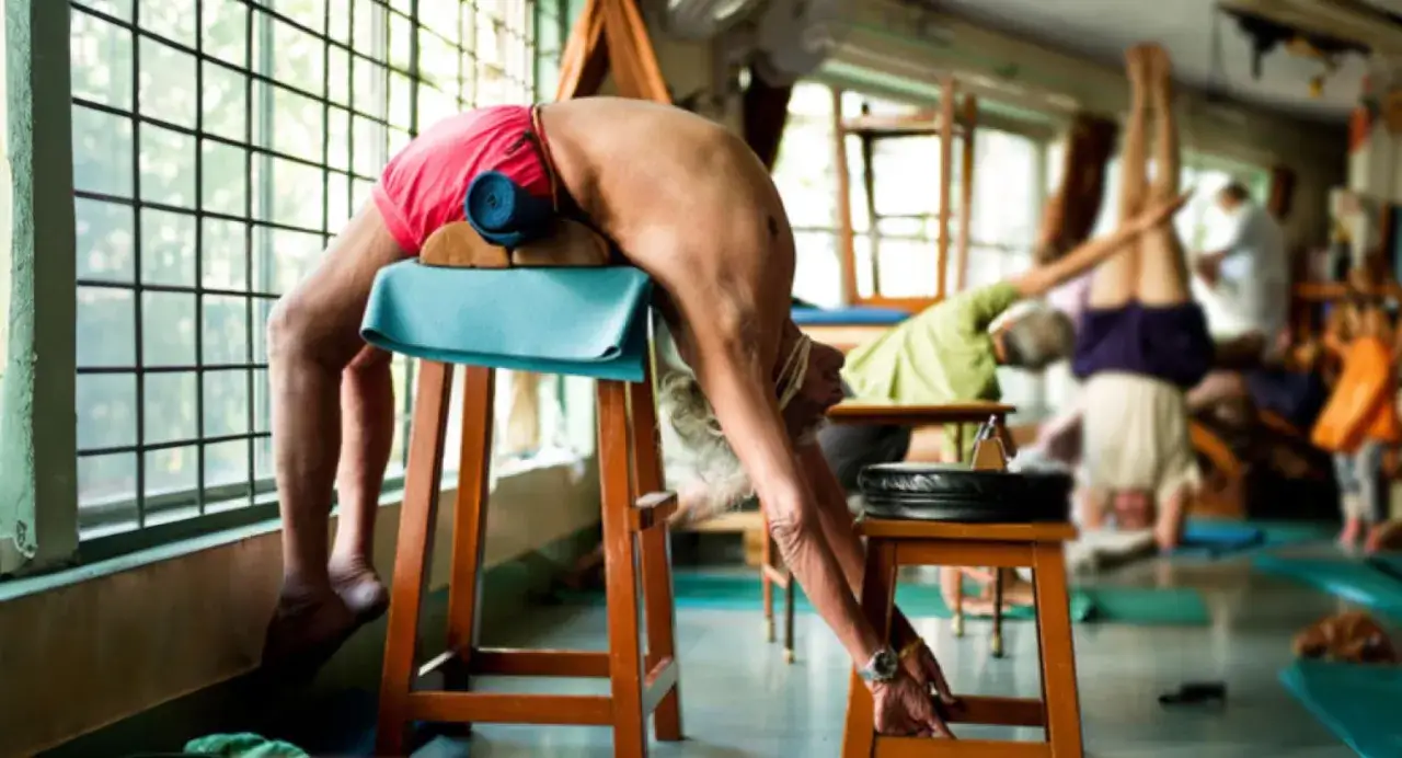 Tiefe R&uuml;ckbeuge mit Hilfsmitteln, ein Mann praktiziert Iyengar Yoga Asanas. Im Hintergrund weitere &Uuml;bende.