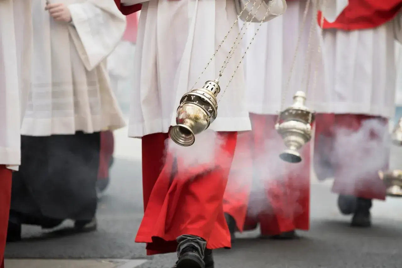 Gl&uuml;hende Weihrauchf&auml;sser steigen auf, w&auml;hrend Geistliche in roten und wei&szlig;en Gew&auml;ndern, wie bei einer Zeremonie unter Summorum Pontificum, durch den Rauch schreiten.