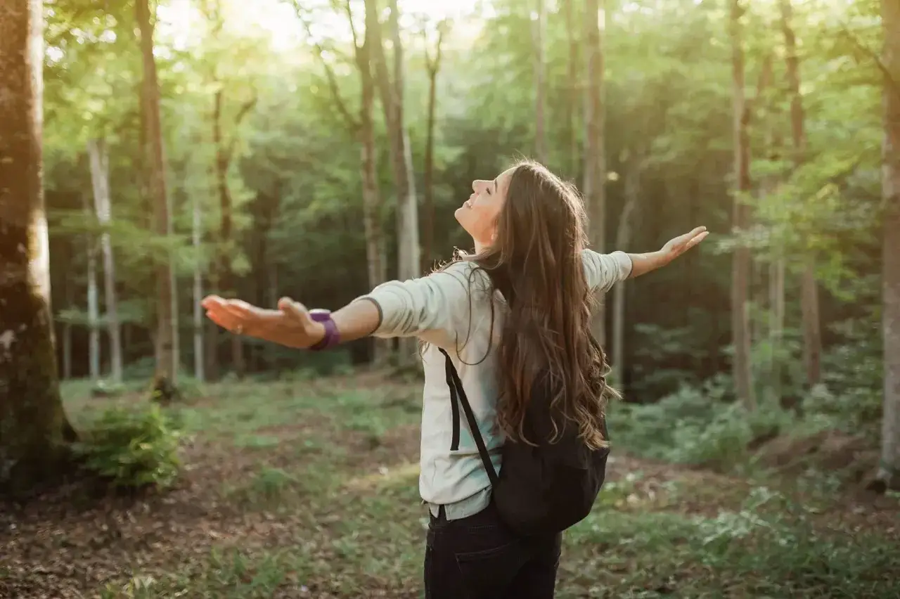 Eine energetische Person mit ausgebreiteten Armen genie&szlig;t die Sonne im Wald.