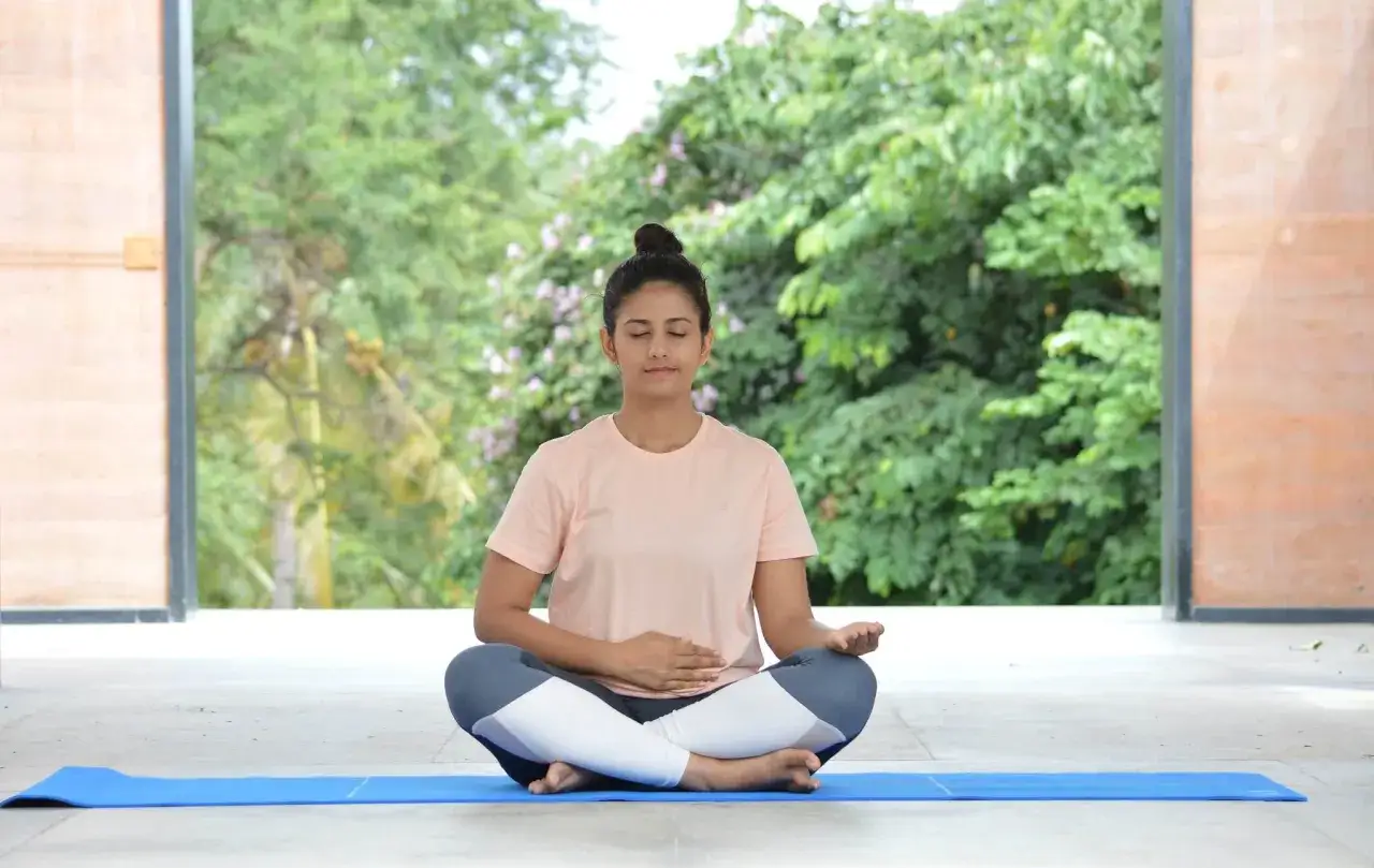 Frau praktiziert Kapalabhati Pranayama im Freien, mit geschlossenen Augen und einer Hand auf dem Bauch.