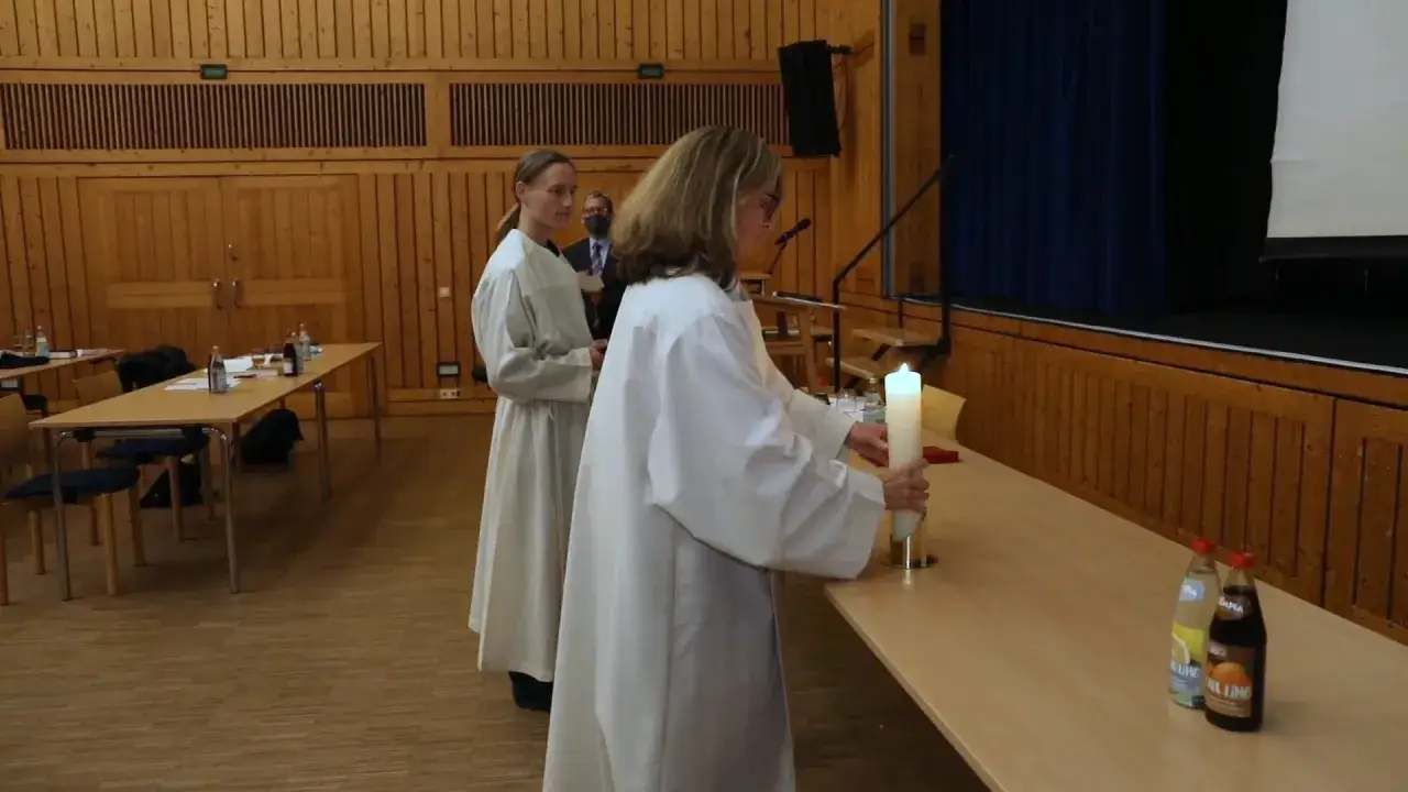 Zwei Personen in wei&szlig;en Gew&auml;ndern bereiten sich auf das Stundengebet des katholischen Priesters vor. Eine Person h&auml;lt eine brennende Kerze.