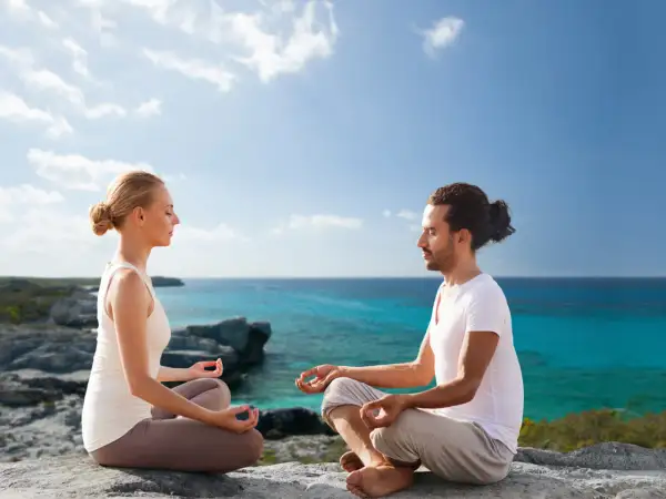 Ein Paar meditiert in Lotusposition an einer felsigen Küste. Sie suchen nach spirituellen Ausbildungen, um ihre innere Ruhe zu finden.