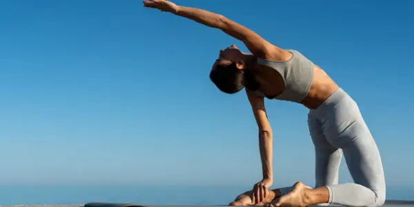 Frau in Yoga-Pose, ideal für Yoga Einsteiger, dehnt sich am Meer unter blauem Himmel.