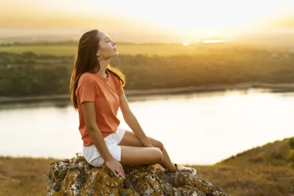 Junge Frau genießt den Sonnenuntergang auf einem Felsen, ein Bild für ein sorgenfreies Leben.