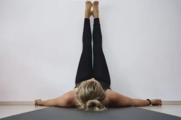 Frau in schwarzer Kleidung praktiziert Yoga Sommer, Beine an der Wand, entspannt auf der Matte liegend.