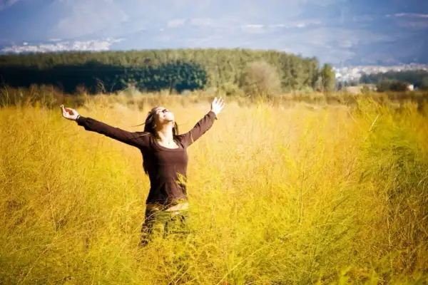 Frau mit ausgebreiteten Armen in einem goldenen Feld, die den Himmel umarmt. Ein Gefühl von Freiheit und der 7. Sinn spirituell.