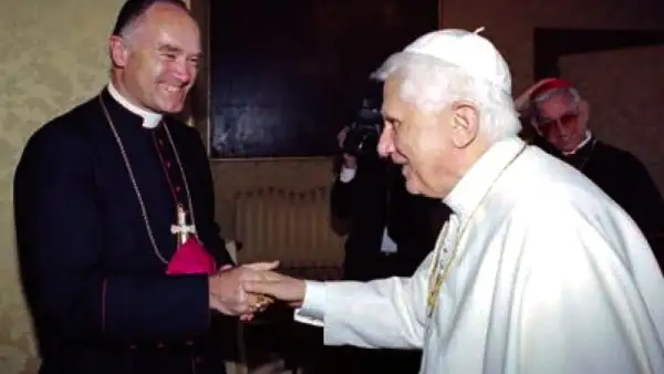 Papst Benedikt XVI. schüttelt einem Bischof die Hand. Im Hintergrund ein Kameramann und ein weiterer Geistlicher, ein Zeichen der Würde der summorum pontificum.