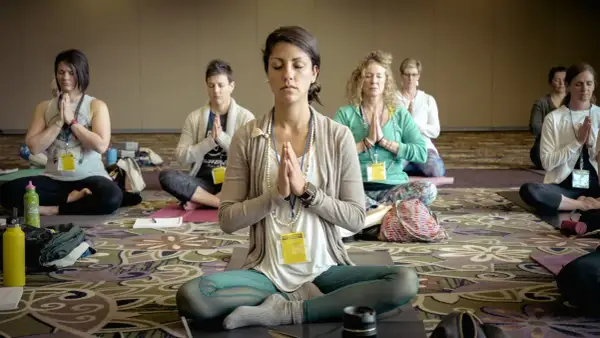 Frauen in einer Gruppe praktizieren transzentale Meditation, sitzen im Schneidersitz mit gefalteten Händen und geschlossenen Augen.