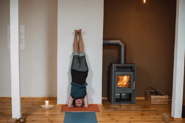 Person in einer Kopfstand-Pose, eine der vielen Iyengar Yoga Asanas, übt vor einem Kaminfeuer.