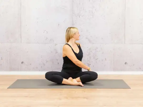 Frau in schwarzer Kleidung praktiziert Yoga-Drehsitz auf einer Matte. Ihre positive Ausstrahlung gibt Motivation für Yoga.