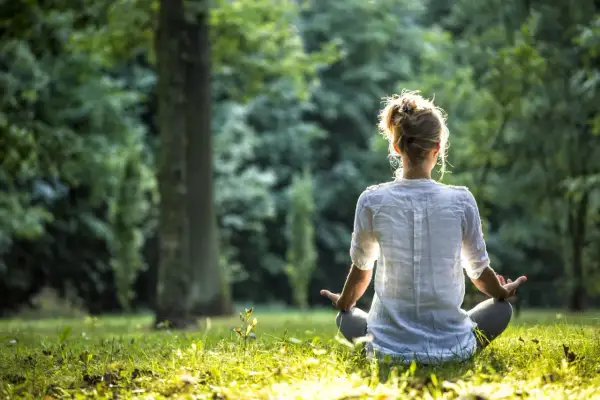 Frau in weißem Hemd meditiert im Wald. Sie nutzt eine Meditation Mantra Liste zur inneren Ruhe.