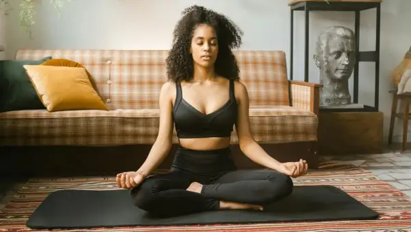 Frau in schwarzer Sportkleidung praktiziert Krafttier Meditation auf einer Matte. Sie sitzt im Lotussitz, Augen geschlossen, Hände im Mudra.