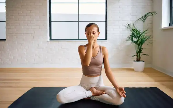 Frau praktiziert Pranayama Atmung im Lotussitz auf einer Yogamatte. Sie hält ihren Finger vor die Nase, um abwechselnd durch die Nasenlöcher zu atmen.