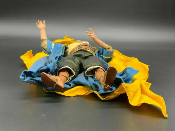 Eine Krippenfigur des heiligen Josef liegt erschöpft auf einem blauen und gelben Tuch.